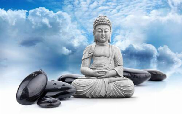 Будда в позе лотоса среди черных камней на фоне лазурного неба