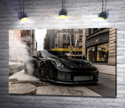 Угольно-черный автомобиль Порше (Porsche) 911 среди улицы старого города