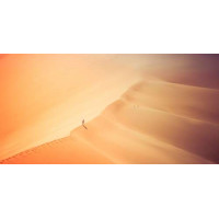 Одинокий силуэт человека, идущего по гребню дюны в бескрайней пустыне