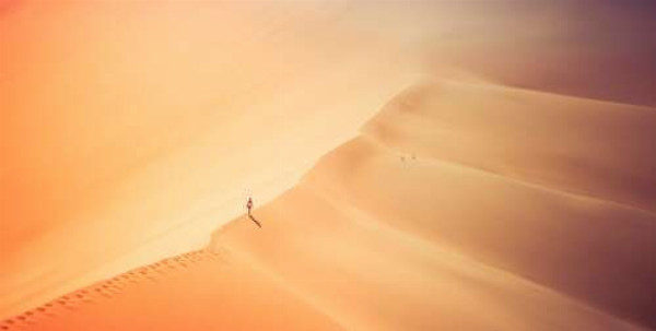 Самотній силует людини, що йде по гребеню дюни в безкраїй пустелі