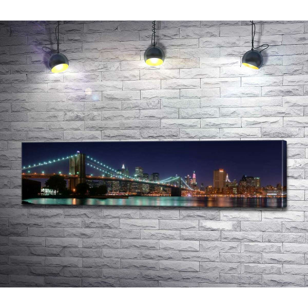 Гирлянды фонарей Бруклинского моста (Brooklyn Bridge) отражаются в водах пролива Ист-ривер (East River)