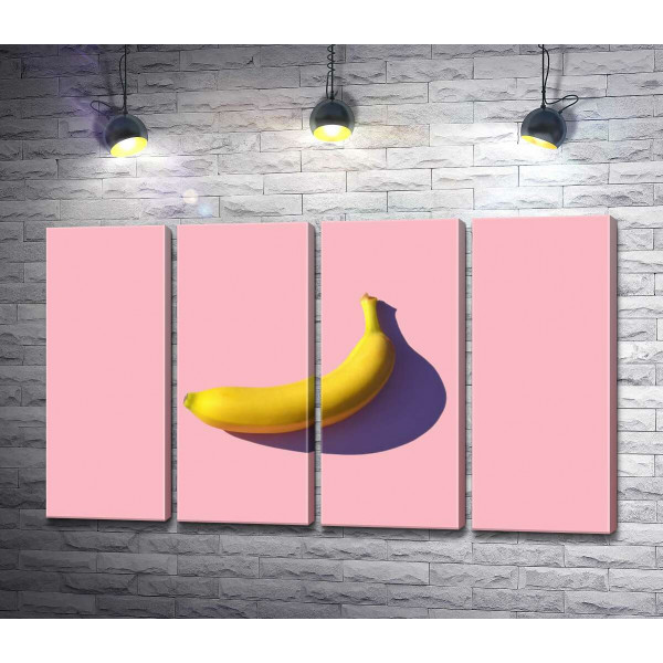 Солнечного цвета банан бросает фиолетовую тень на розовый фон