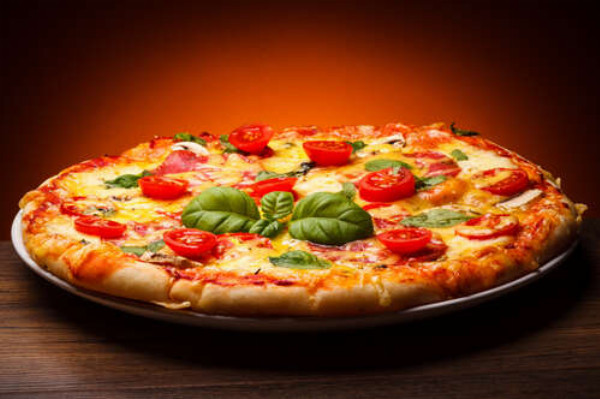 Пишний шар тіста в піці, оздобленій слайсами помідорів та базиліком