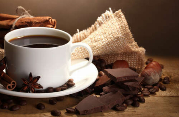 Чашка кофе в окружении пряностей, шоколада и орехов