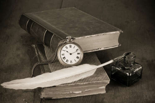 Кишеньковий годинник сперся на старі книги поряд з чорнильницею та пером
