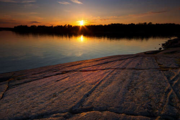 Вечернее солнце бросает лучи на каменный берег реки