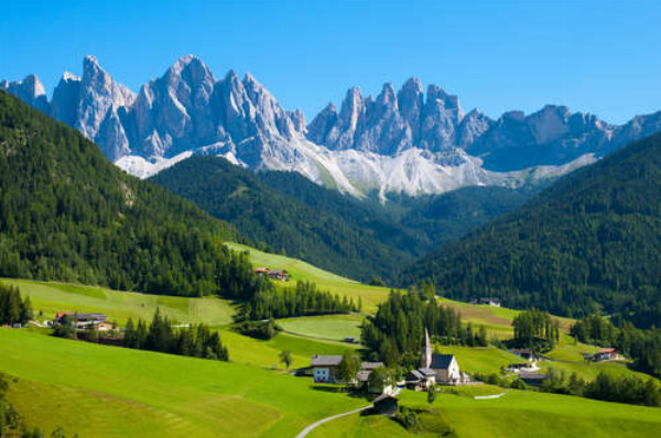 Альпійське село заховалось на зеленій рівнині серед засніжених гірських шпилів 