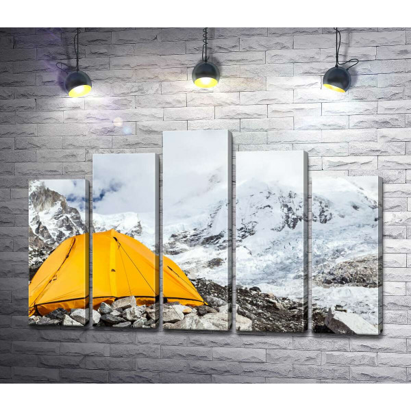 Желтая палатка стоит у заснеженной горной вершины