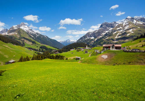 Маленькая деревня стоит среди зеленых сочных альпийских лугов