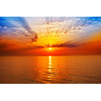 Оранжевое солнце образует арку лучей в небе над морем
