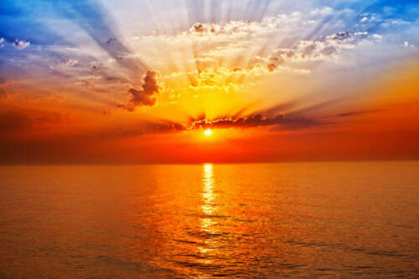 Оранжевое солнце образует арку лучей в небе над морем