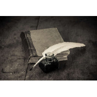 Элегантное белое перо лежит на старой книге рядом со стеклянной чернильницей