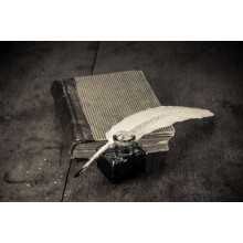 Елегантне біле перо лежить на старій книзі поряд зі скляною чорнильницею