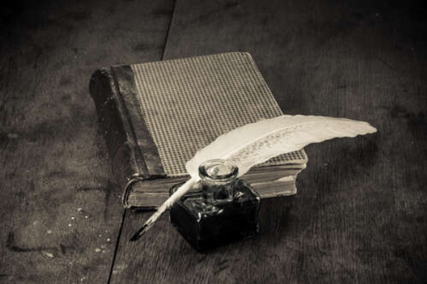 Елегантне біле перо лежить на старій книзі поряд зі скляною чорнильницею