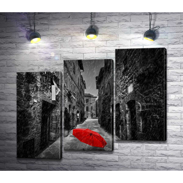 Красный зонтик лежит на дождливой улице старого города