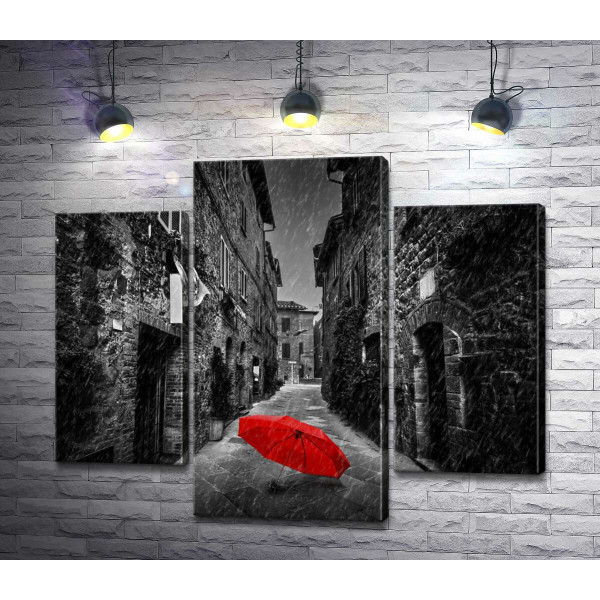 Красный зонтик лежит на дождливой улице старого города