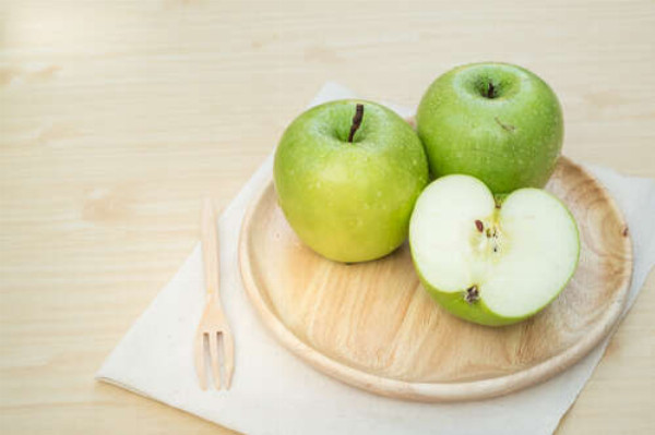 Зелені стиглі яблука на дерев'яній тарілці
