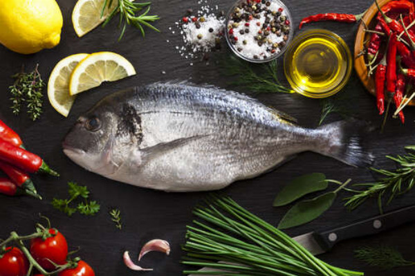 Свіжа риба дорадо в оточенні овочів та спецій
