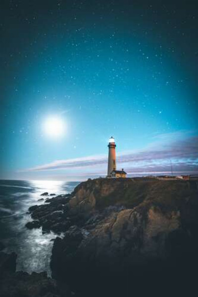 Белое сияние луны освещает маяк на высоком скалистом берегу