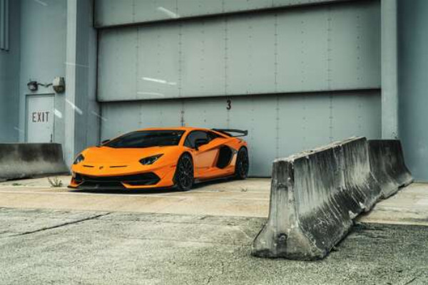 Помаранчевий автомобіль Lamborghini Aventador біля ангара