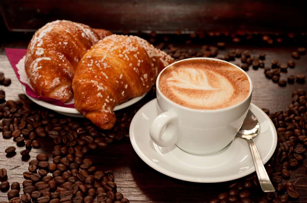 картина-постер Золотистые круассаны и горьковатая терпкость капучино в белой чашке среди кофейных зерен