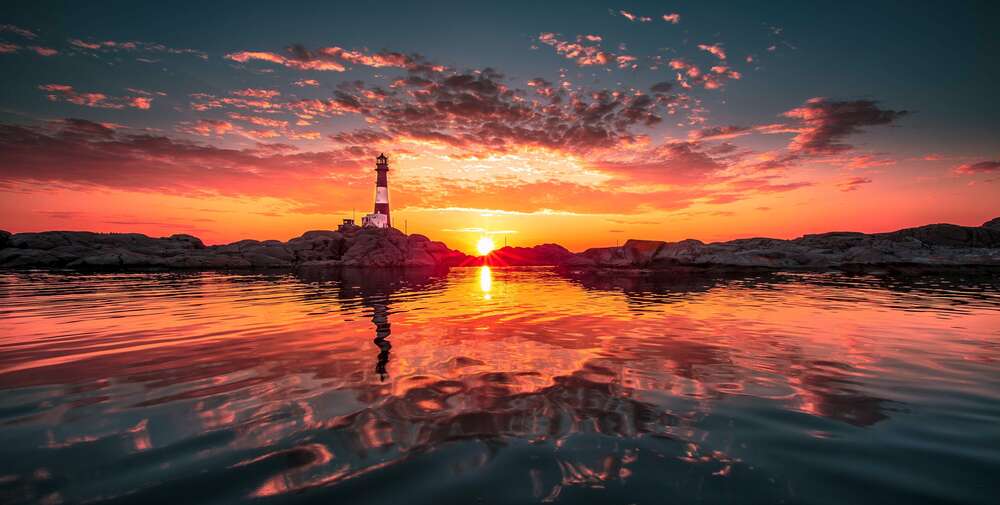 картина-постер Силуэт маяка на скалистом берегу в оранжевом свете солнца