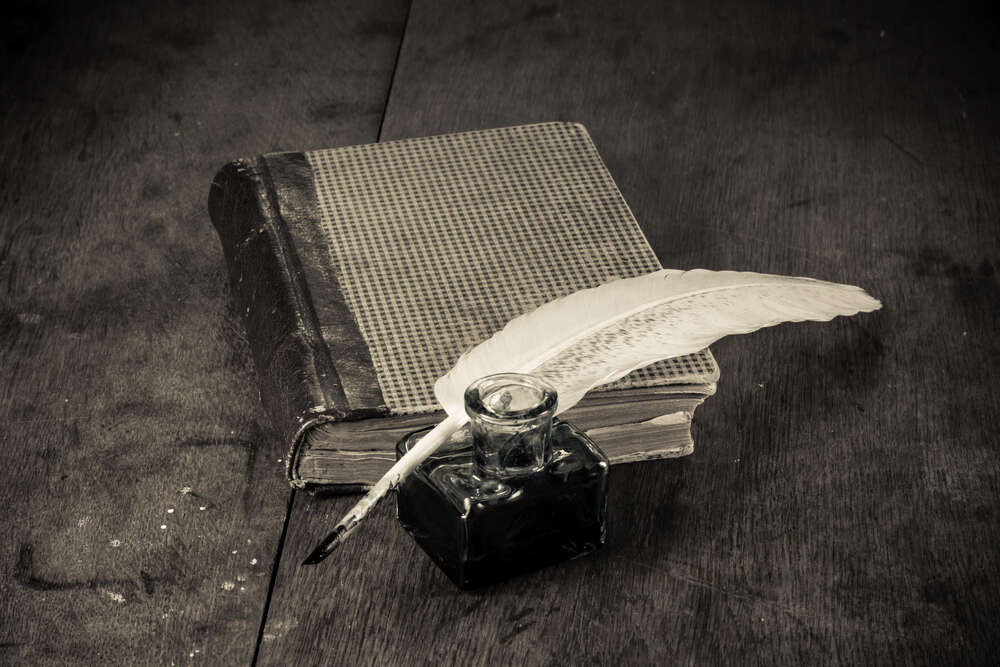 картина-постер Елегантне біле перо лежить на старій книзі поряд зі скляною чорнильницею